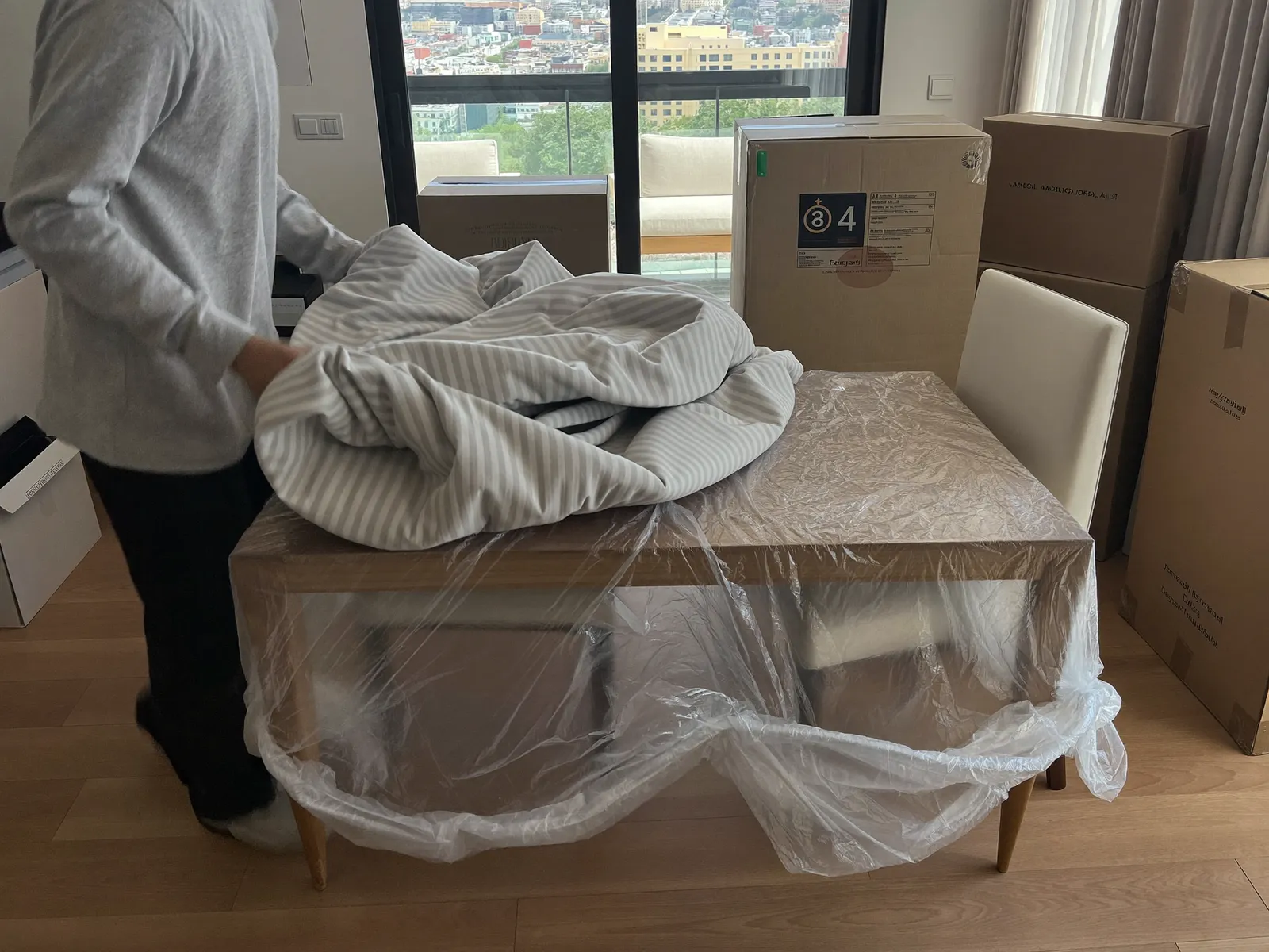 Mover wrapping a dining table in blankets and stretch film in a Dubai apartment